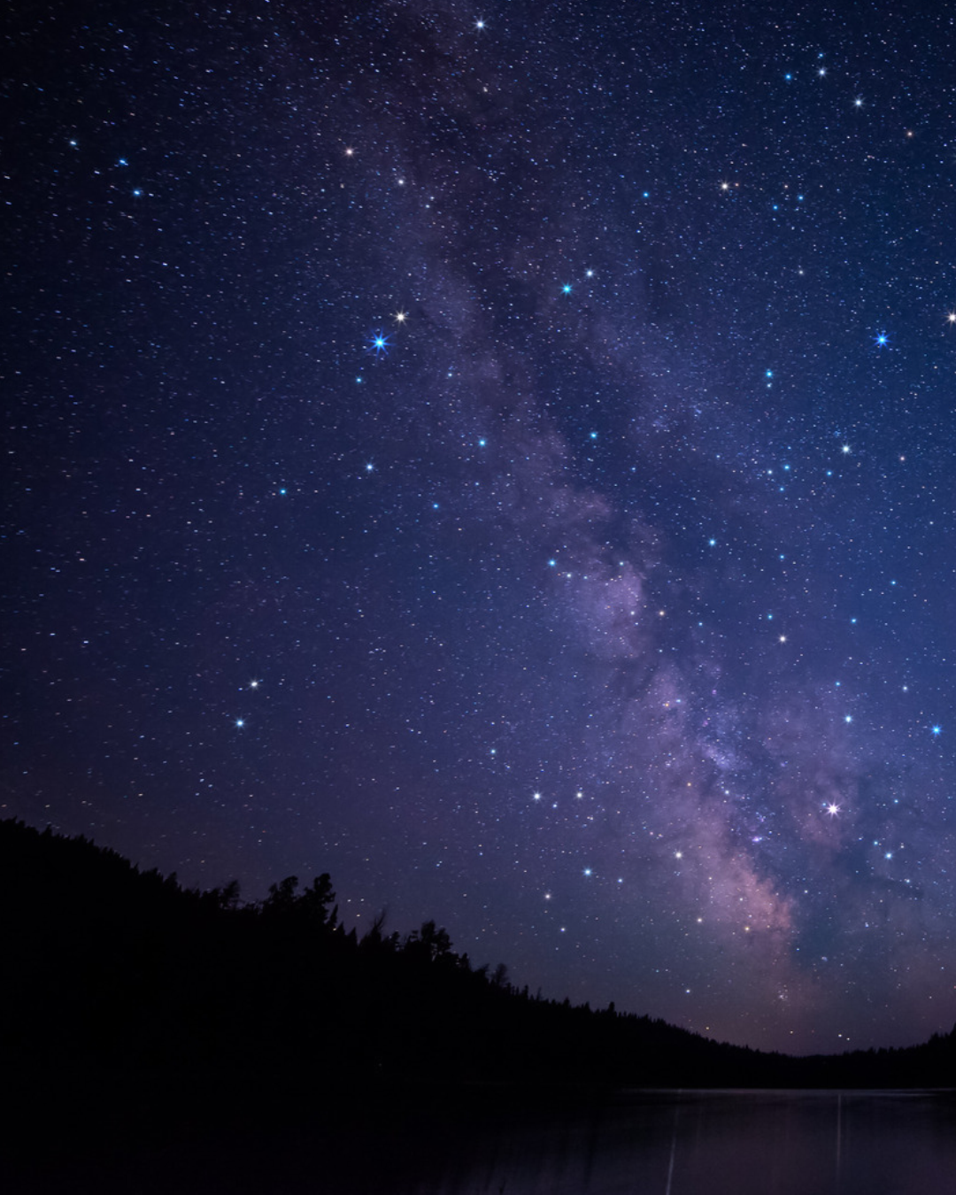 The science of darkness: the Milky Way across a star-filled night sky above a forested ridge and a still lake